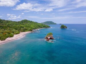 Aerial view of a secluded tropical beach and turquoise coastline in Costa Rica surrounded by lush green forest and small rocky islands.